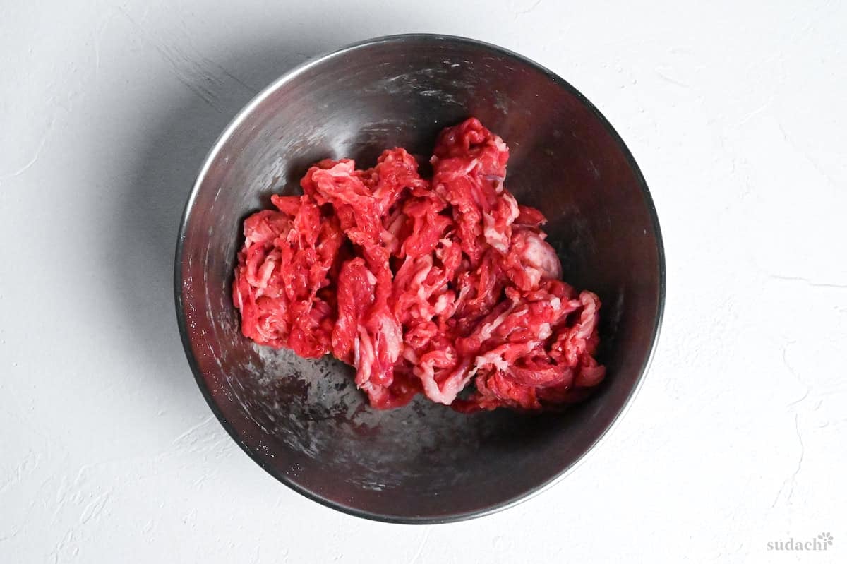 thinly sliced beef in a steel mixing bowl