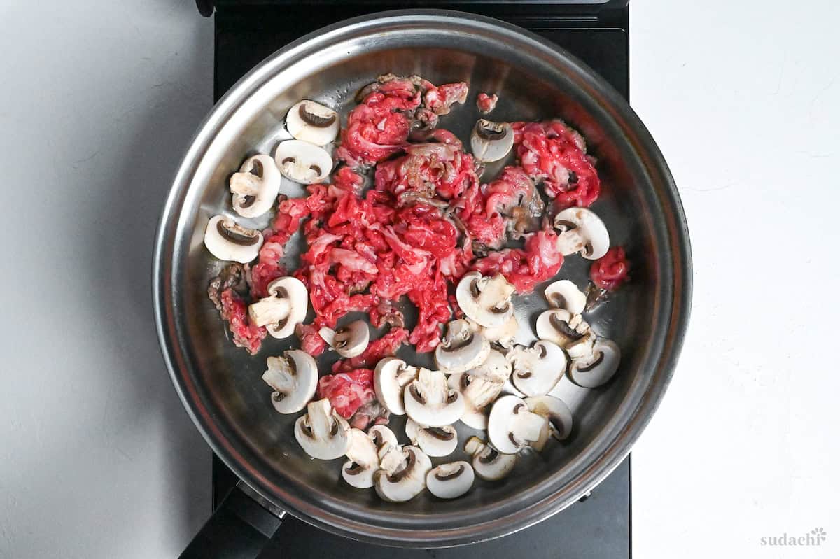 beef and sliced button mushrooms frying in a pan