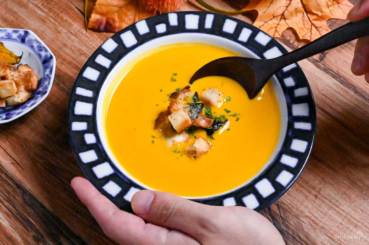 Japanese style kabocha soup in a white bowl with blue patterned rim, scooped with a wooden spoon
