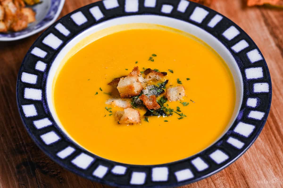 Japanese style kabocha soup topped with homemade croutons and kabocha skin in a white bowl with blue patterned rim close up