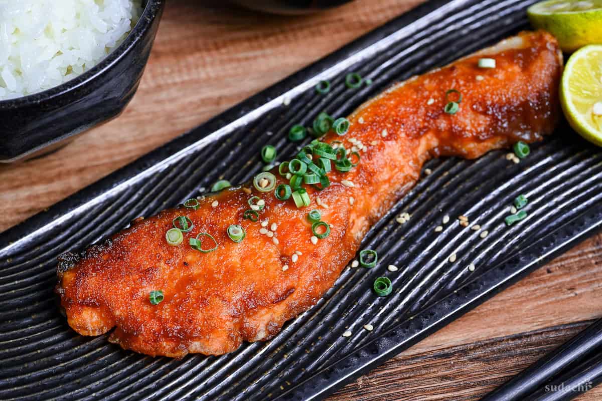 Miso glazed salmon on a long rectangular black plate with a wave design