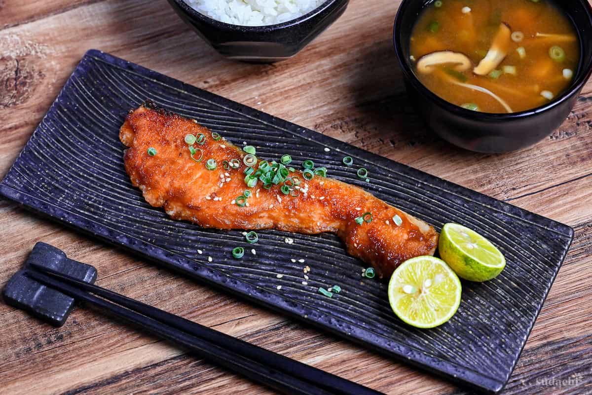 Miso glazed salmon on a long rectangular black plate with a wave design