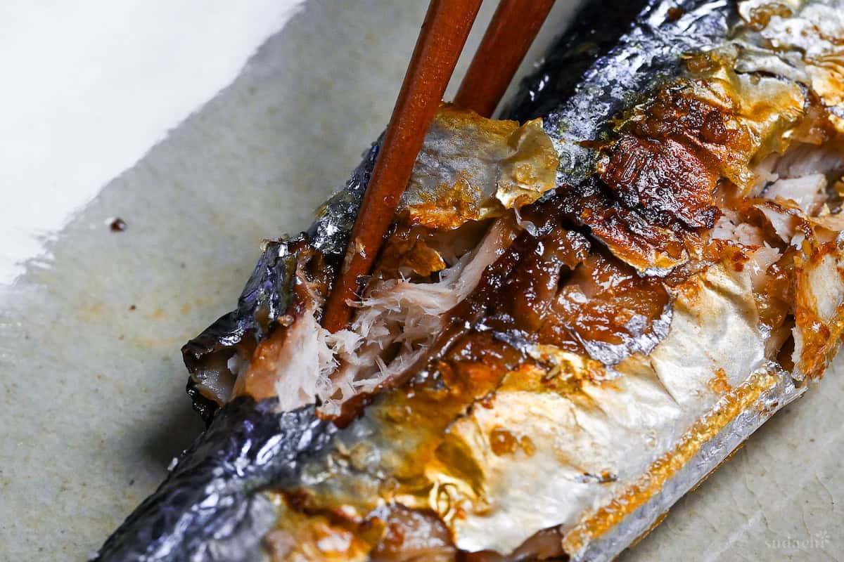 close up of wooden chopsticks breaking into grilled sanma