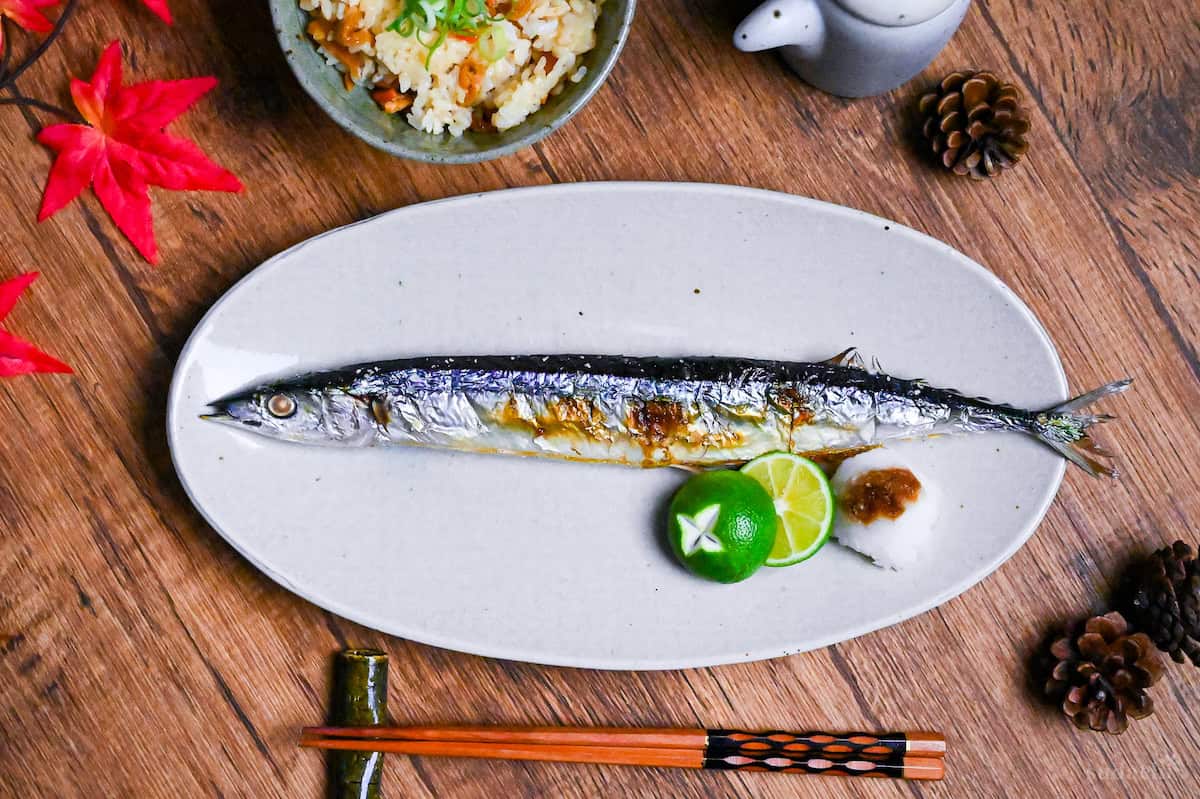 Grilled Sanma (Pacific Saury) on a long off-white oval plate with sudachim grated daikon and a splash of soy sauce