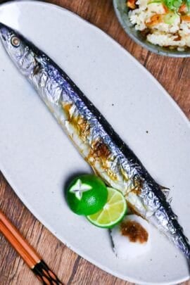 Grilled Sanma (Pacific Saury) on a long off-white oval plate with sudachim grated daikon and a splash of soy sauce