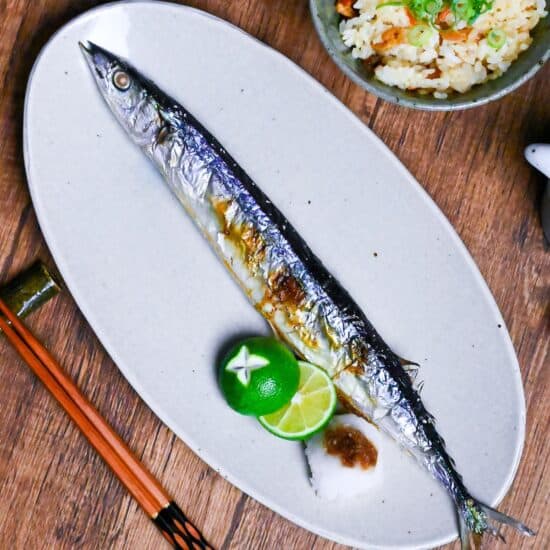 Grilled Sanma (Pacific Saury) on a long off-white oval plate with sudachim grated daikon and a splash of soy sauce