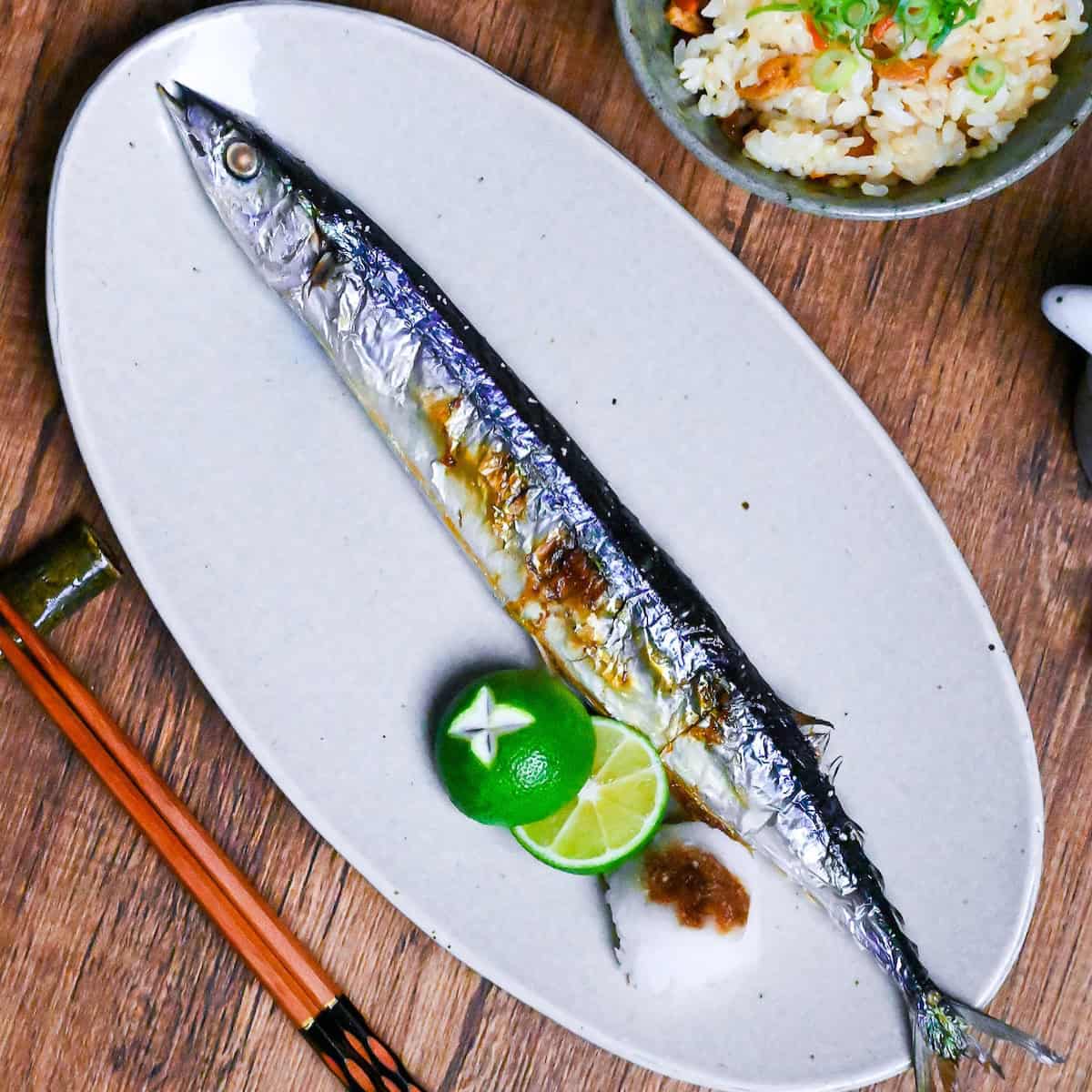 Grilled Sanma (Pacific Saury) on a long off-white oval plate with sudachim grated daikon and a splash of soy sauce