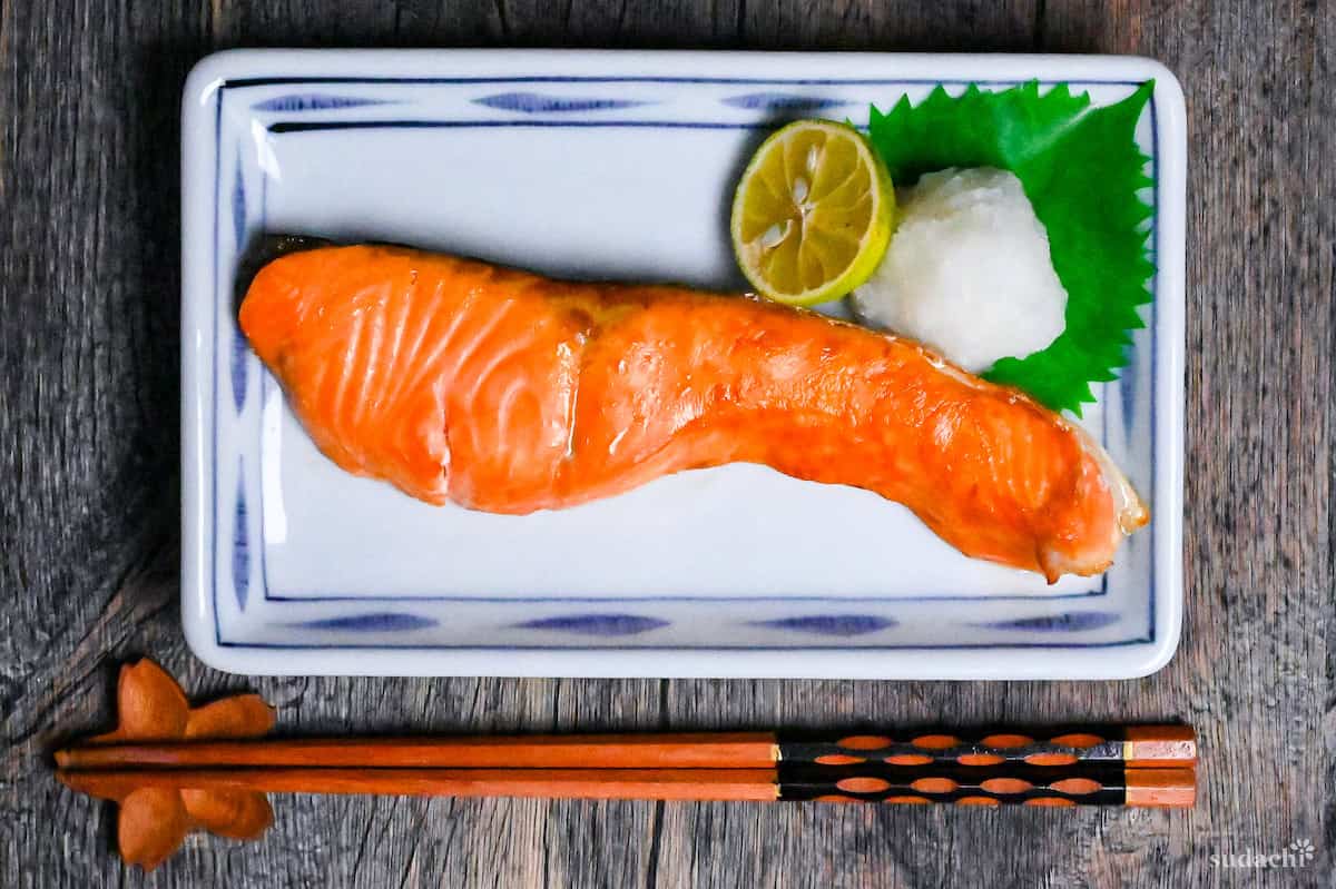 Japanese salt grilled breakfast salmon (shiozake) next to grated daikon and a sudachi on a white plate with blue rim top down