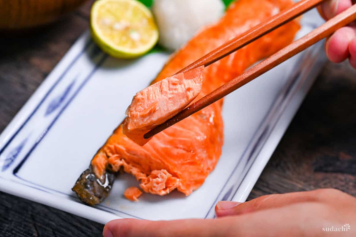 A piece of shiozake (Japanese salted salmon) held up with wooden chopsticks