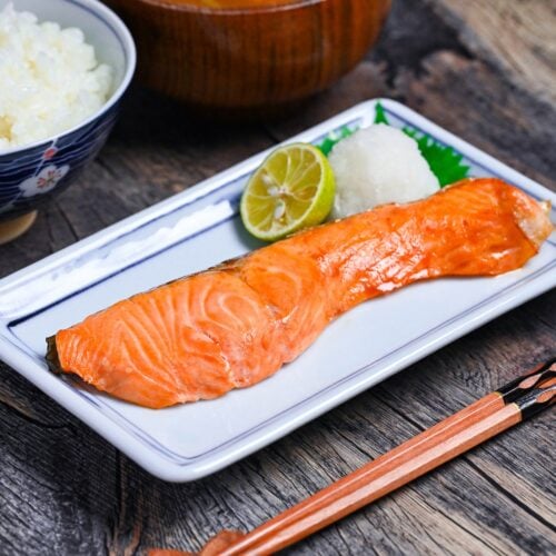 Japanese salt grilled breakfast salmon (shiozake) next to grated daikon and a sudachi on a white plate with blue rim
