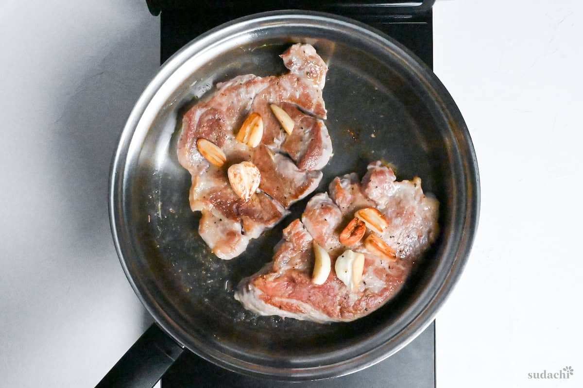 Browned pork steaks and garlic in a stainless steel pan on the stove