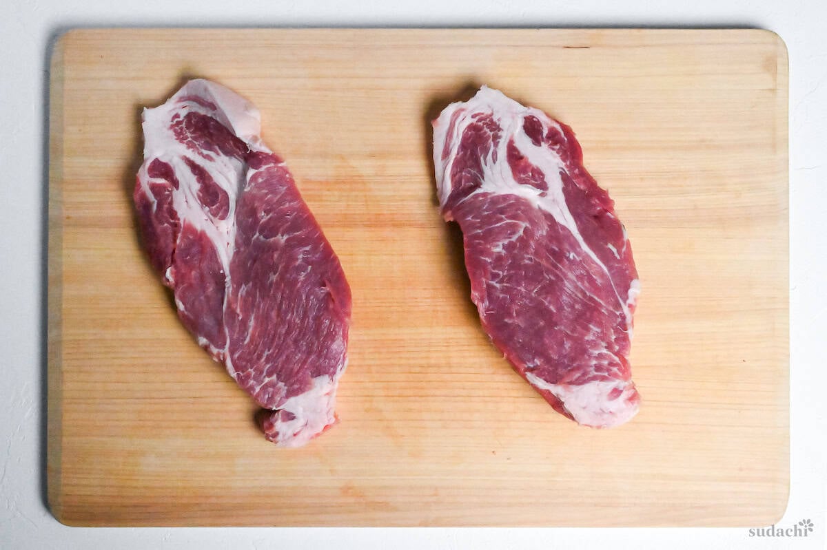 two pork loin shoulder steaks on a wooden cutting board