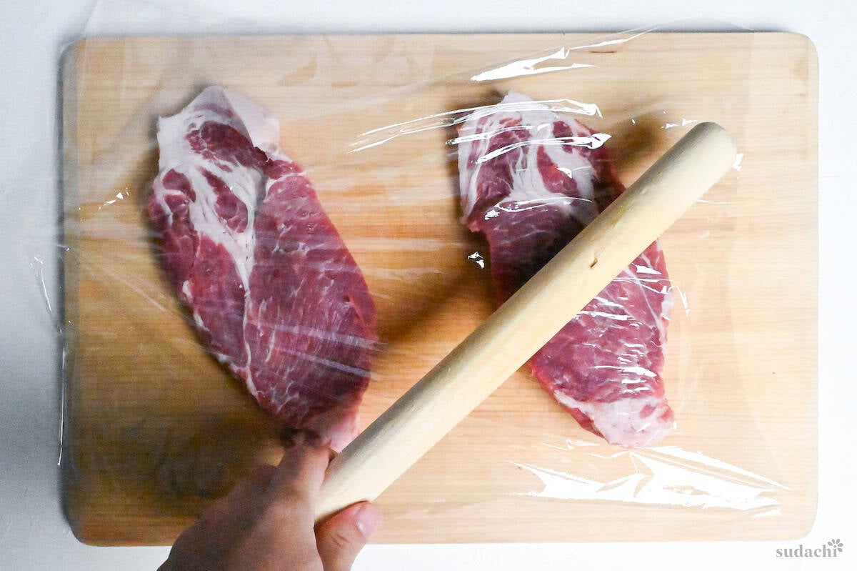 pounding pork shoulder loins with a rolling pin on a wooden cutting board