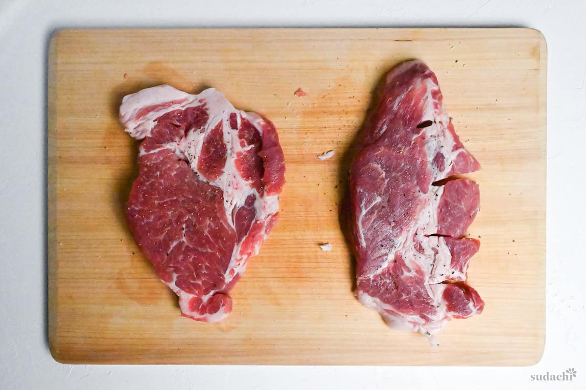 Two tonteki pork steaks sprinkled with salt and pepper on a wooden cutting board