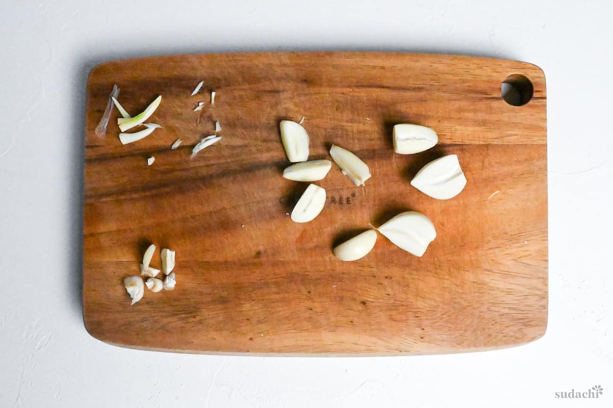 Halved garlic cloves on a wooden cutting board with cores removed