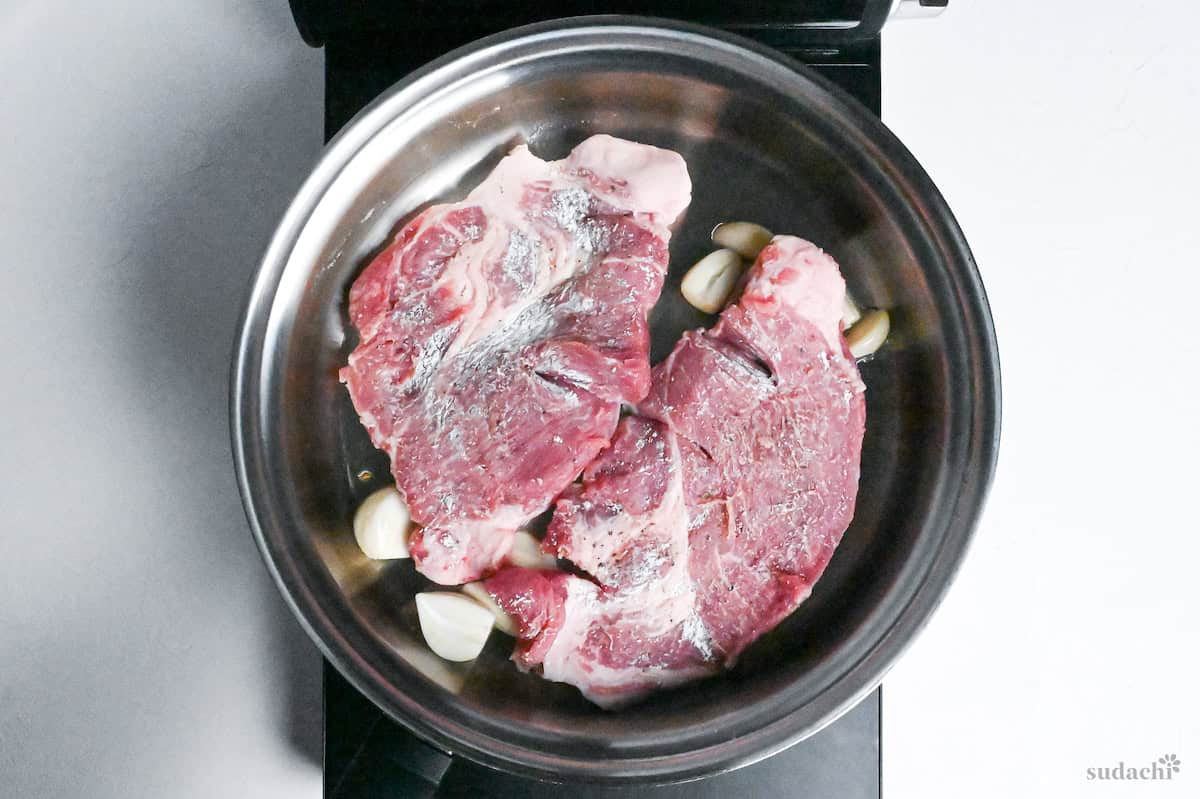 Pork steaks and garlic in a stainless steel pan on the stovetop