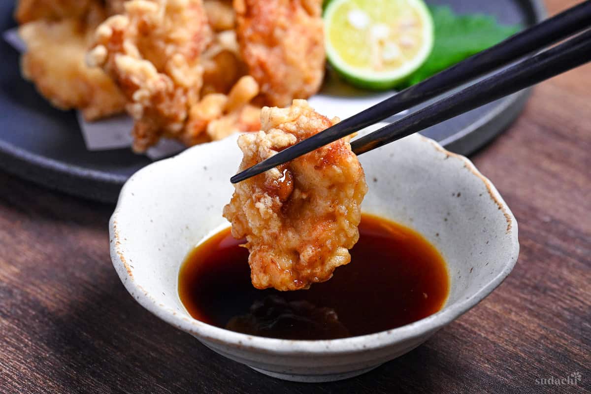 black chopsticks holding chicken tempura and dipping it in citrus soy sauce