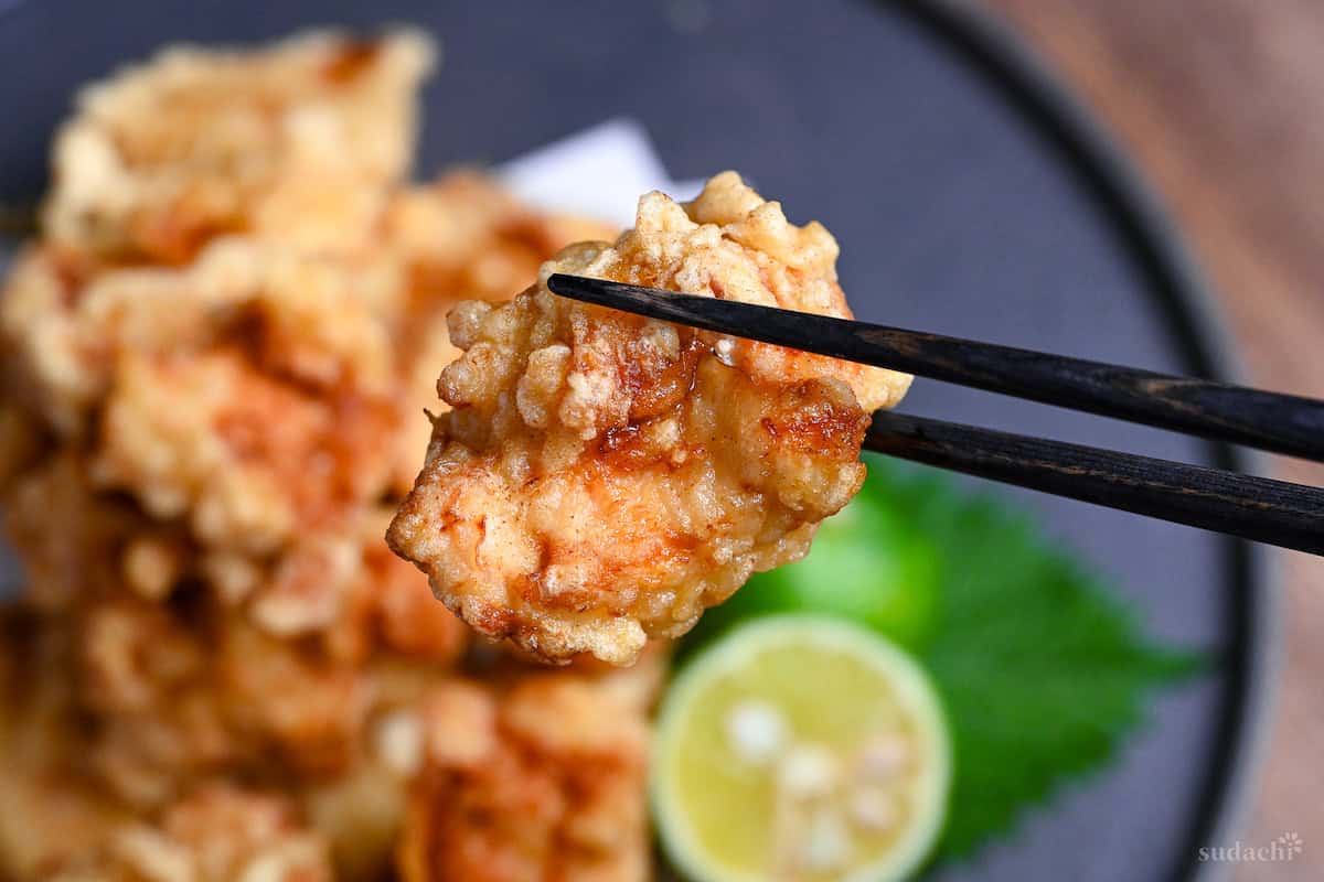close up of chicken tempura held up with black chopsticks