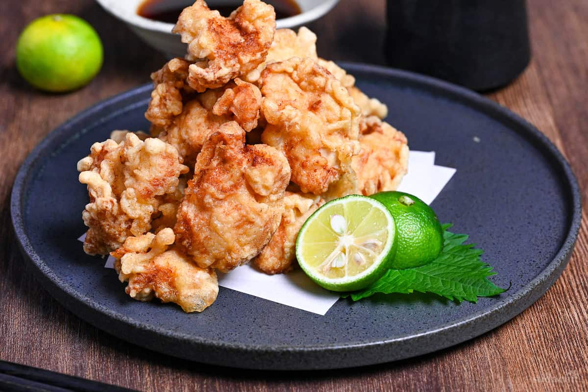 chicken tempura (toriten) on a dark gray round plate next to halved sudachi and shiso leaf