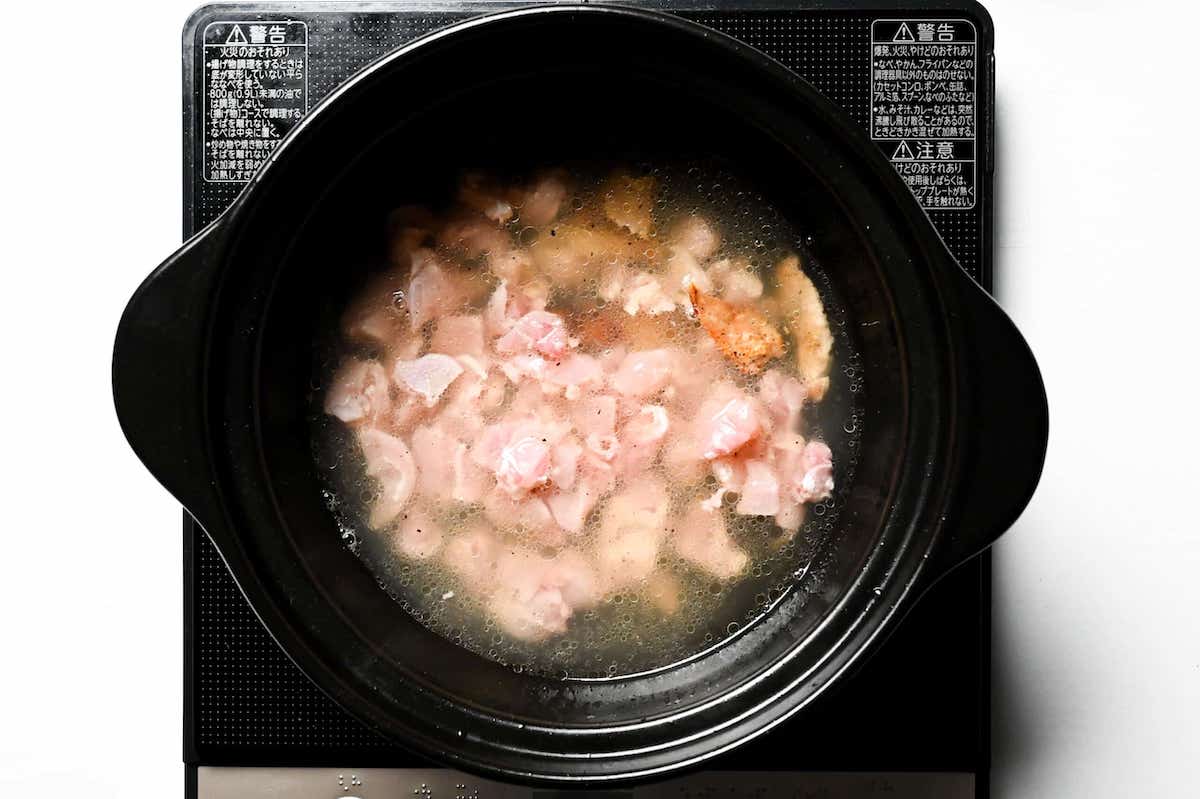 chicken cooking in dashi in a black pot on the stove top
