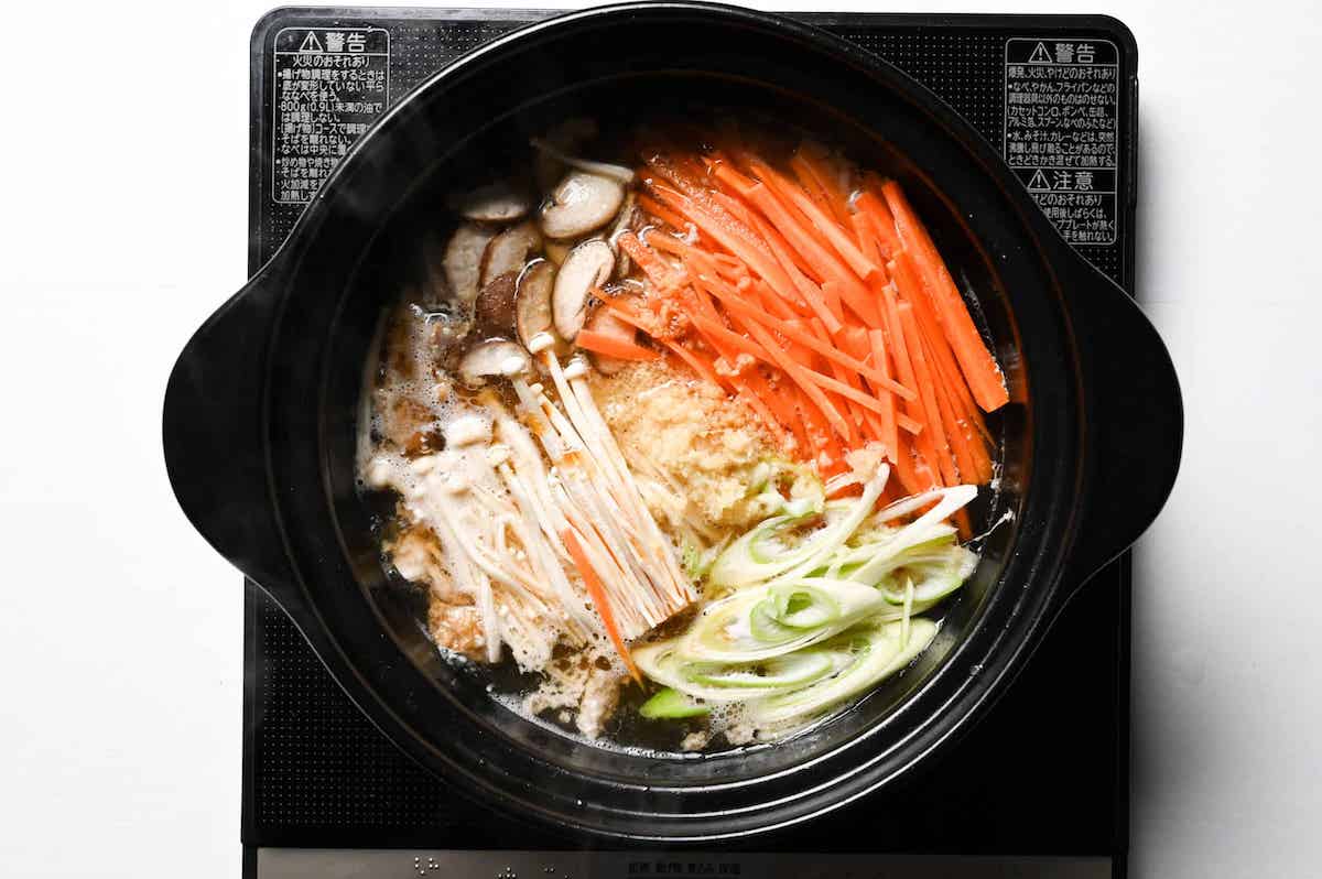 julienned vegetables added to chicken zosui broth in a black pot