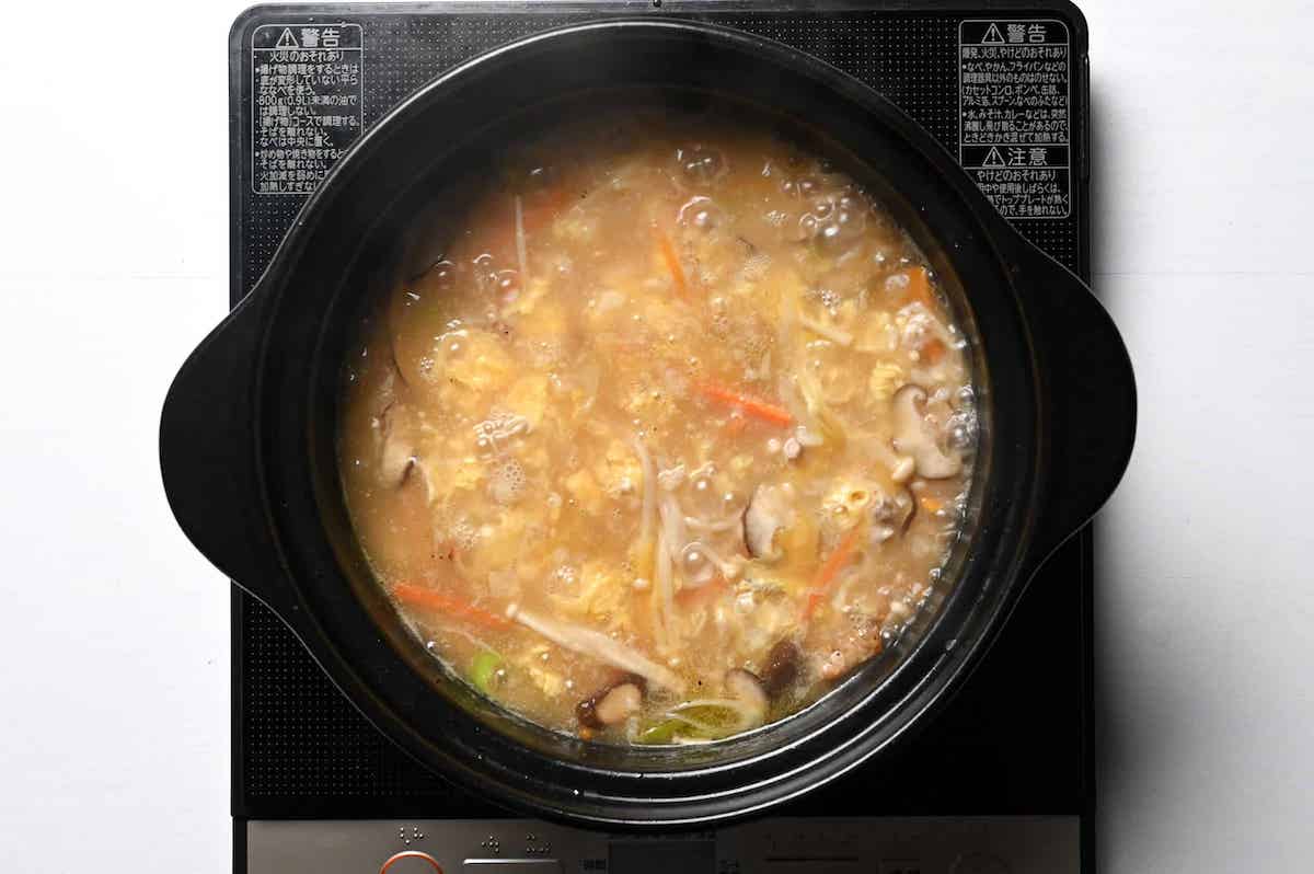 egg added to chicken zosui in a black pot