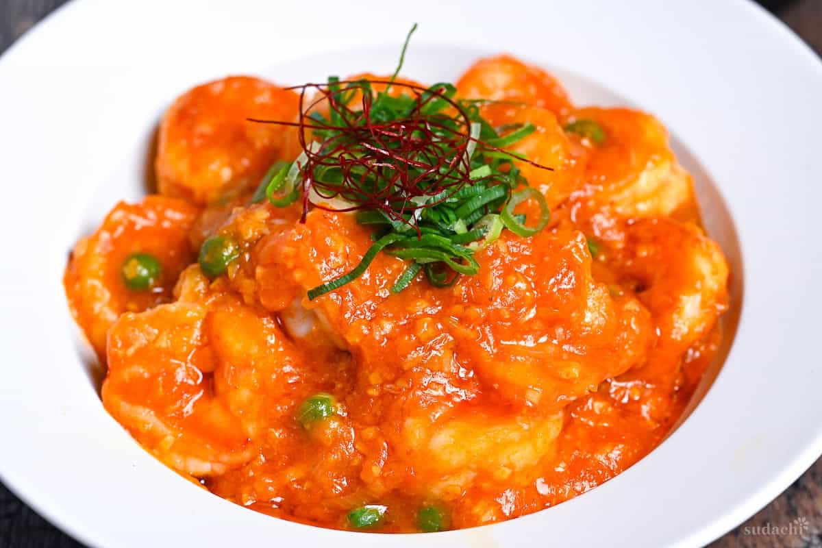 close up of ebi chili topped with chopped green onions, green peas and chili threads in a white dish