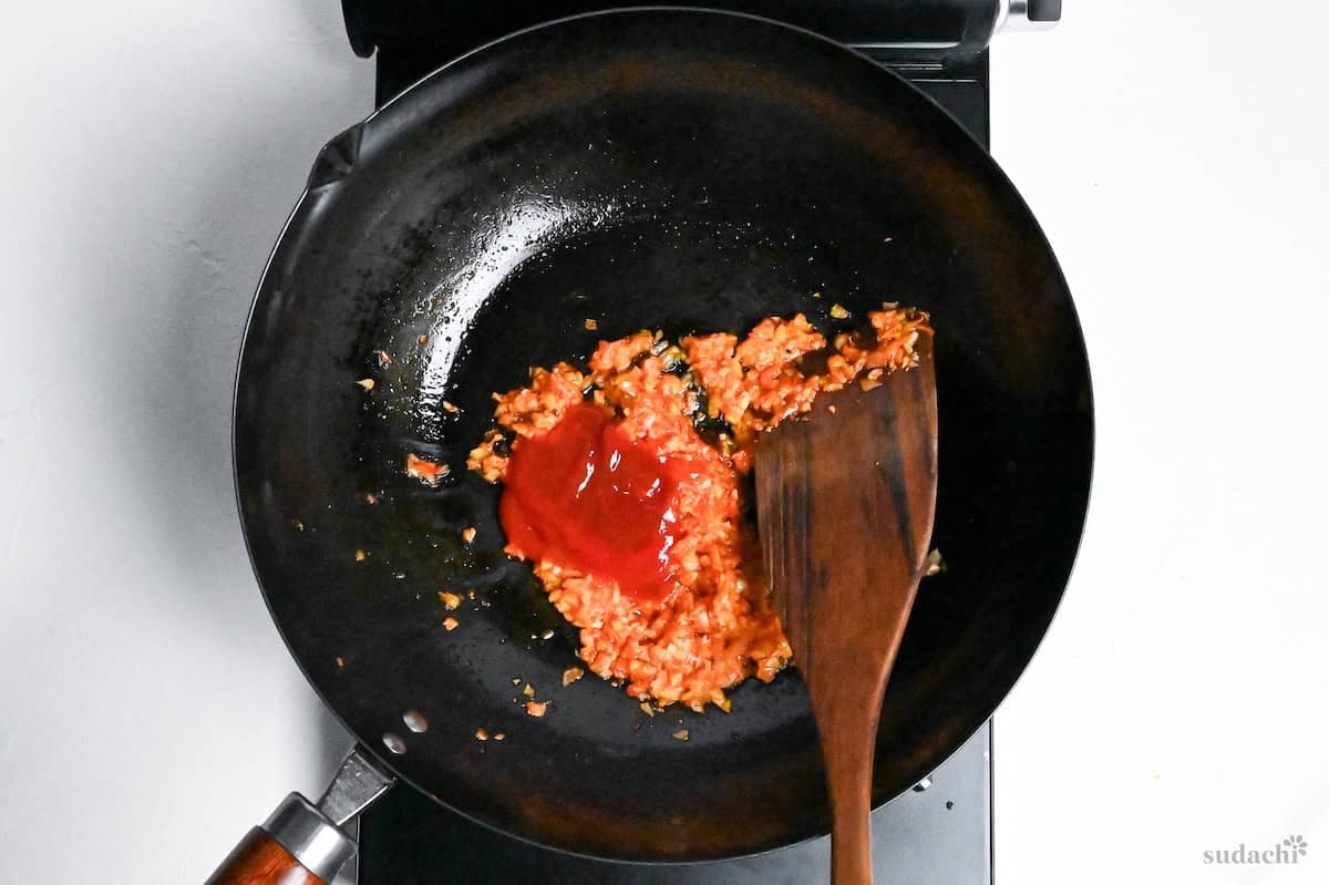 ketchup added to chili bean paste and aromatics in a wok to make ebi chili sauce