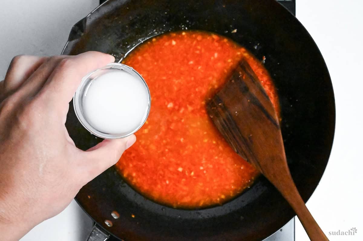 adding a slurry made with cold water and starch to ebi chili sauce in a wok (to thicken)