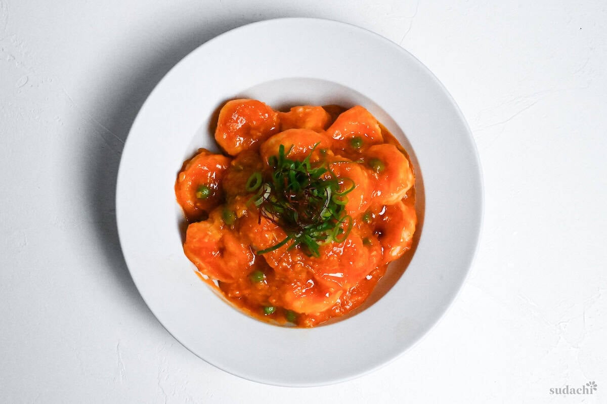 ebi chili in a white bowl topped with green peas, chopped green onion, and chili threads on a white background