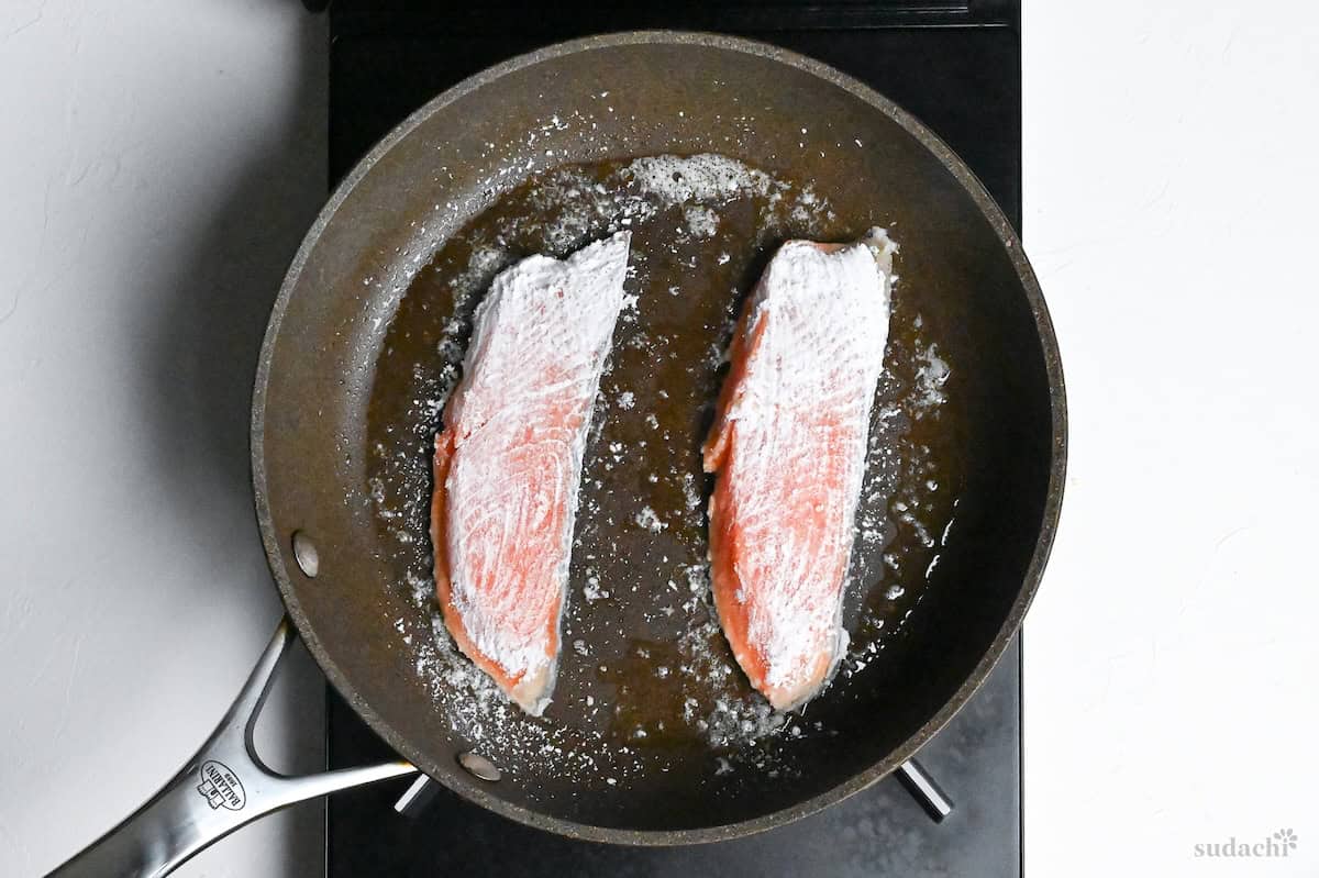 starch coated salmon fillets in a frying pan