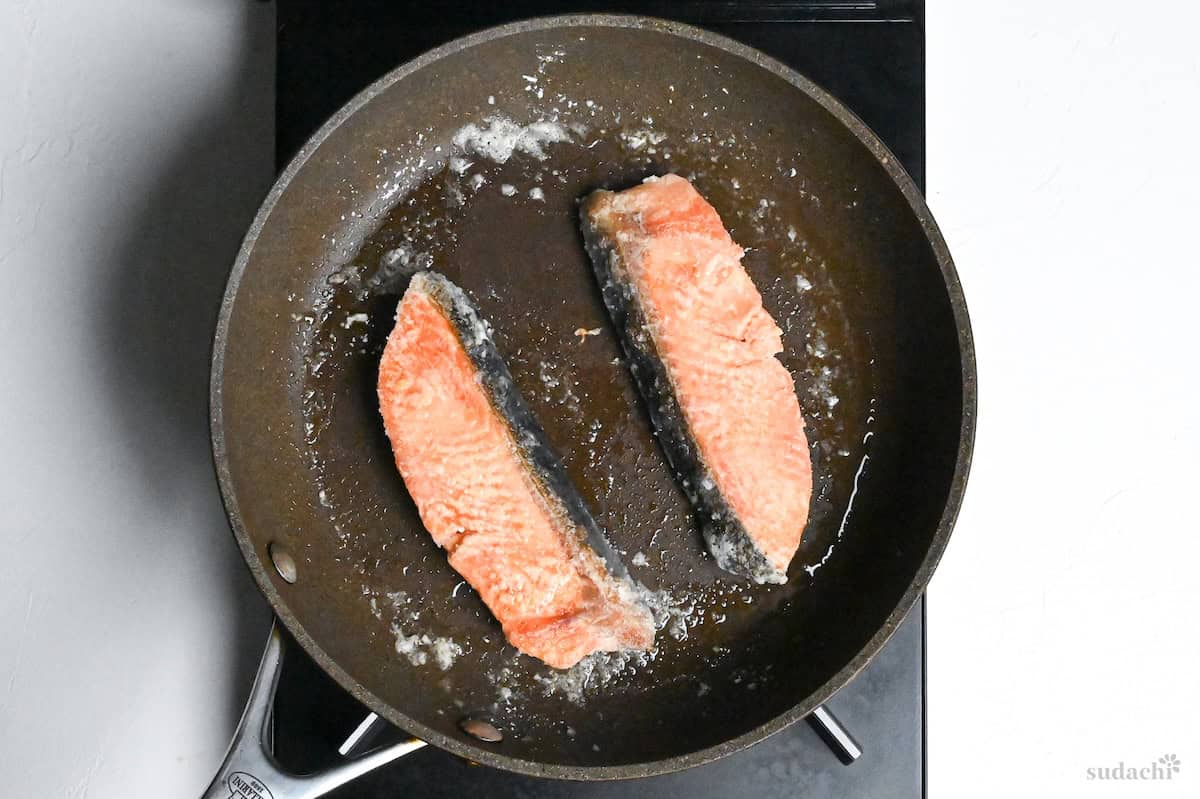 flipped starch coated salmon fillets in a frying pan
