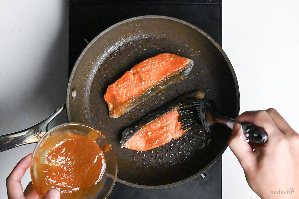 brushing pan fried salmon fillets in a frying pan with miso glaze