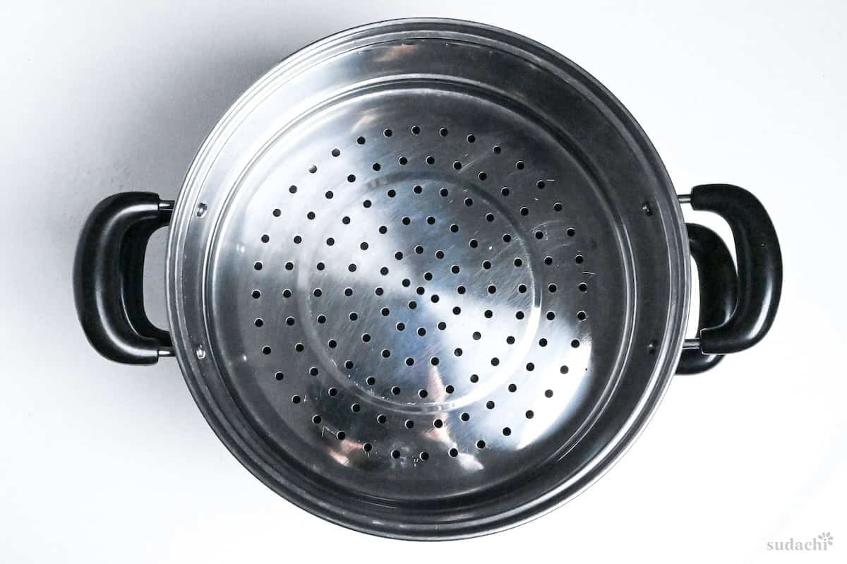 steel steaming basket over pot on a white background