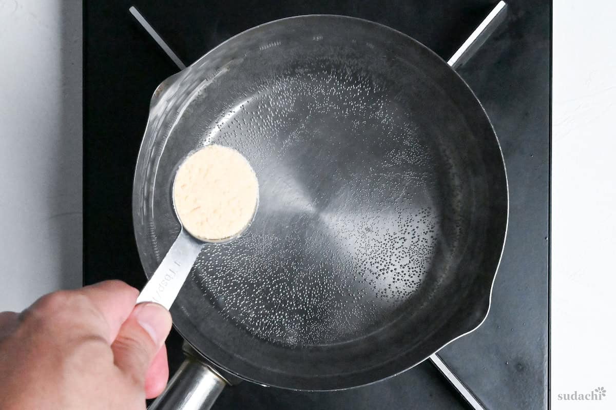 adding Chinese style chicken bouillon powder to kombu dashi in a pot on the stove