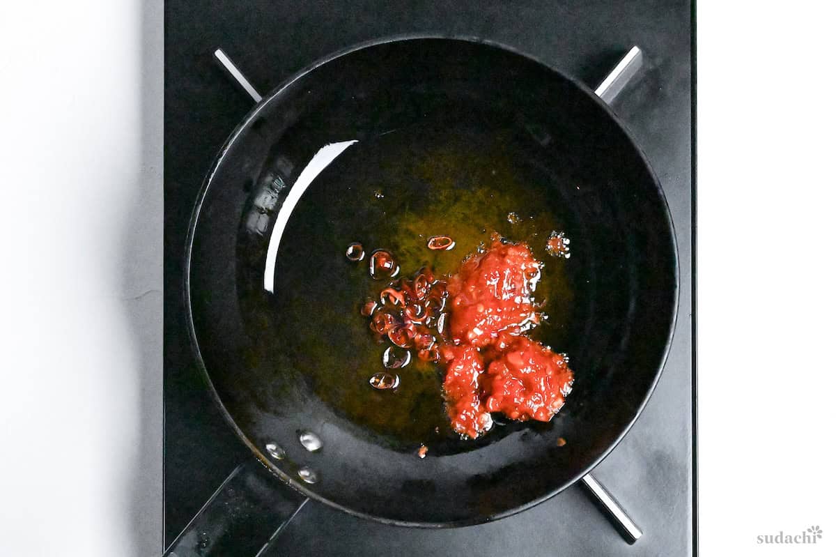 frying Chinese chili bean paste (tobanjan) and dried chilis in an oiled pan on the stove