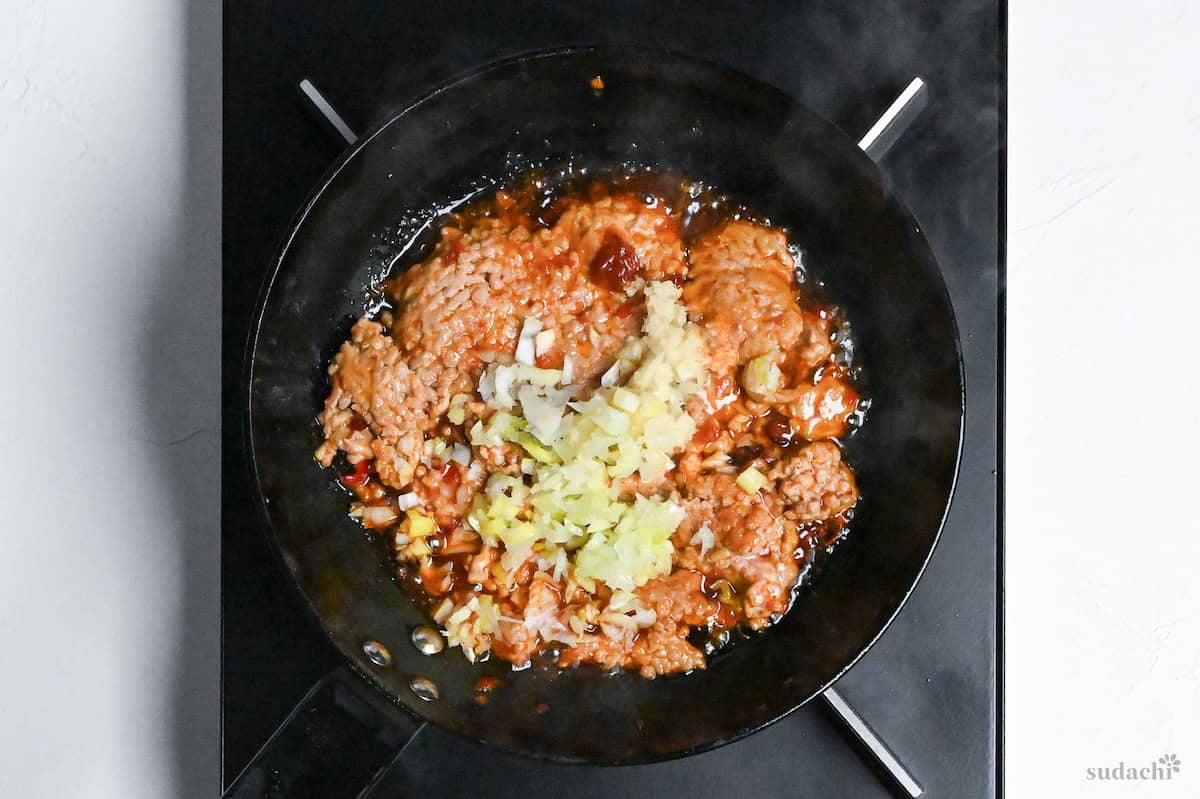 ground pork frying in a pan on the stove with finely diced Japanese leek and grated garlic and ginger