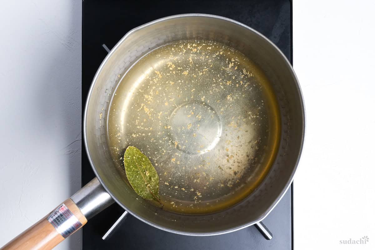chicken stock and bayleaf simmering in a pot on the stove