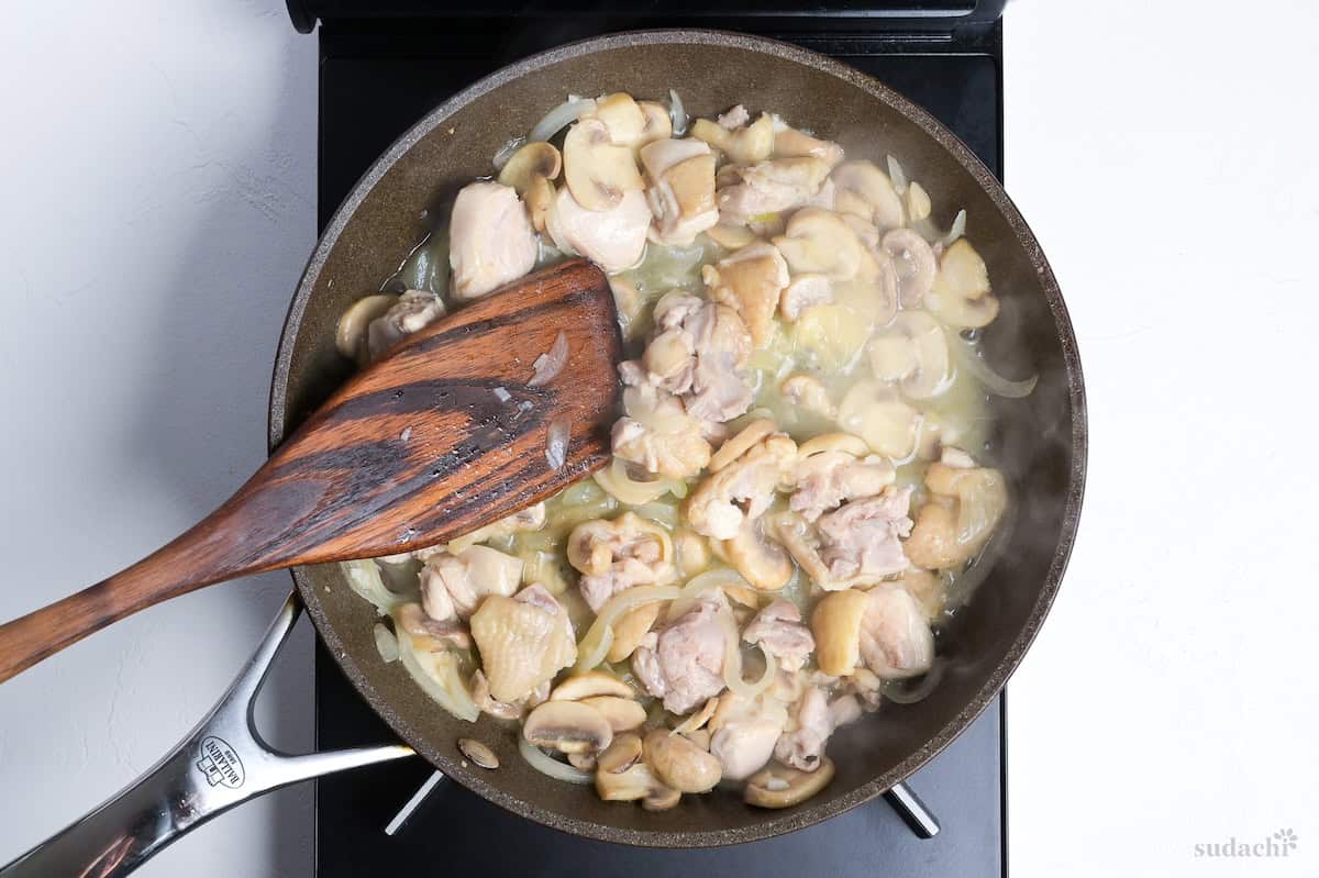chicken and vegetables simmering in stock in a pan on the stove top