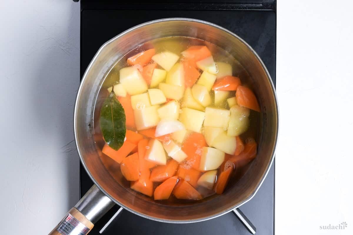carrot and potatoes simmering in chicken stock in a Japanese yukihira pot on the stove top
