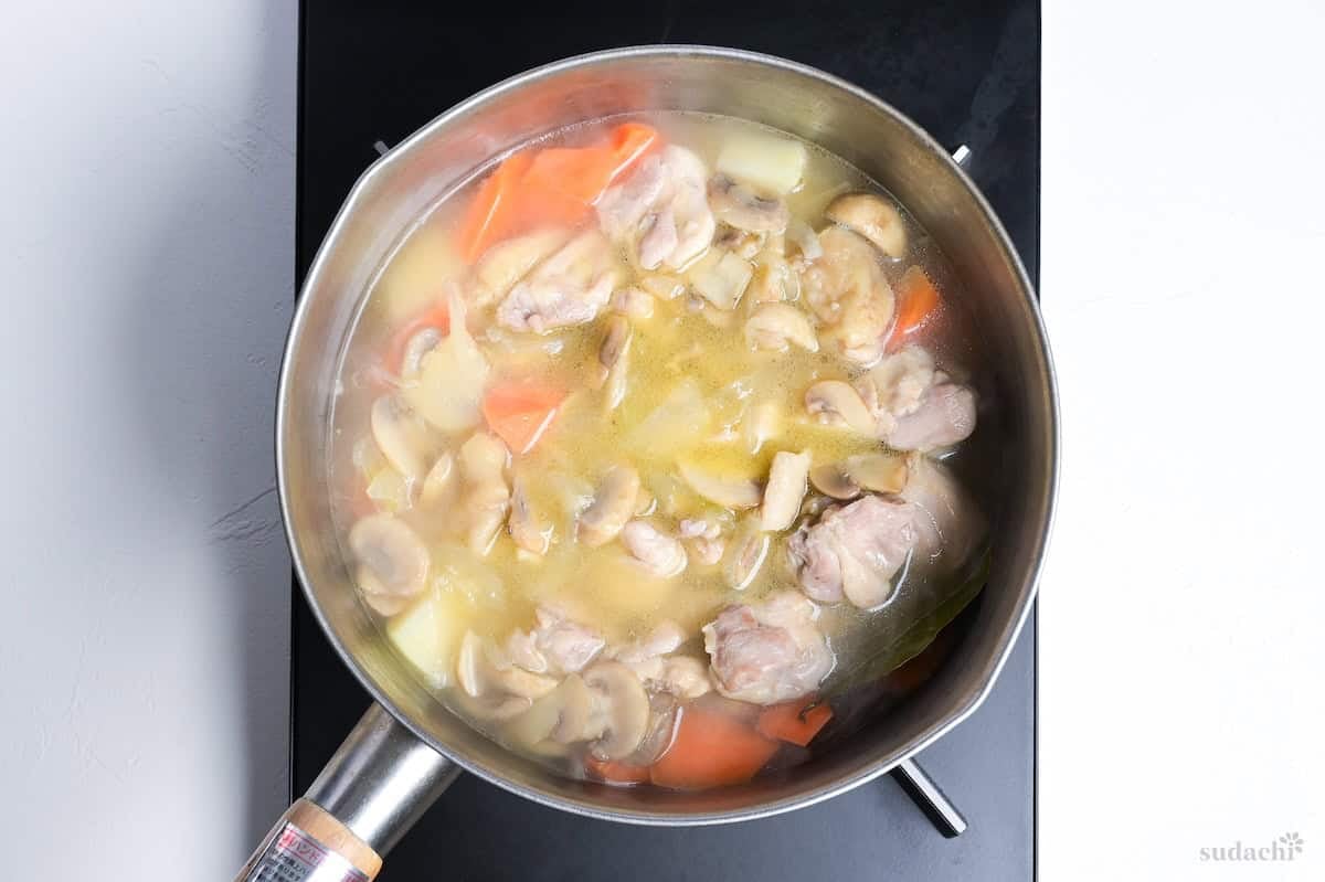 chicken and vegetables simmering in broth in a Japanese yukihira pot on the stove top
