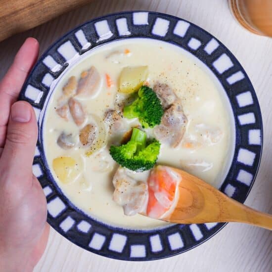 Japanese chicken cream stew in a white bowl with blue and white block patterned rim, with a wooden spoon lifting a scoop with chicken and carrot