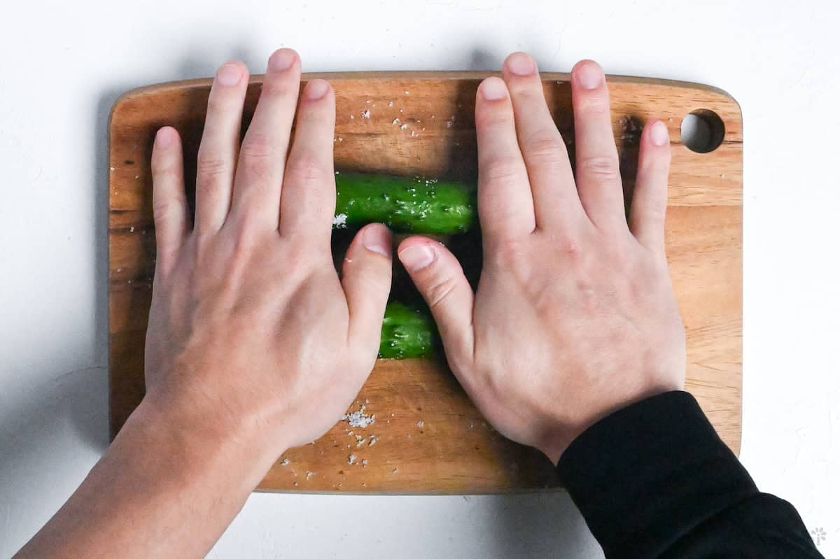 rolling Japanese cucumbers over salt on a wooden cutting board