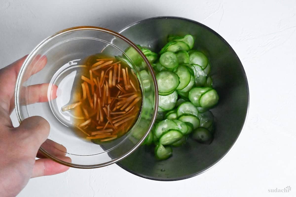 adding marinade and ginger to a bowl of thinly sliced Japanese cucumbers