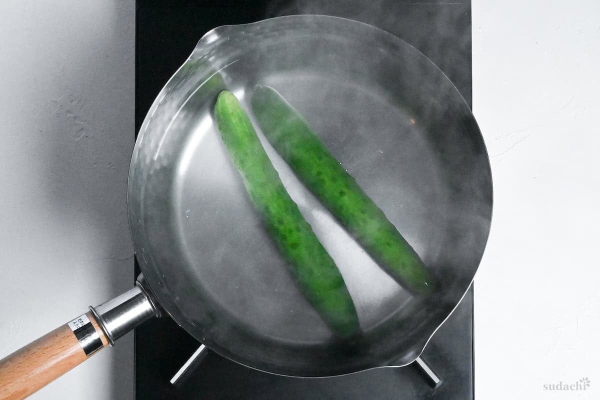 blanching two Japanese cucumbers in a pot of boiling water on the stove