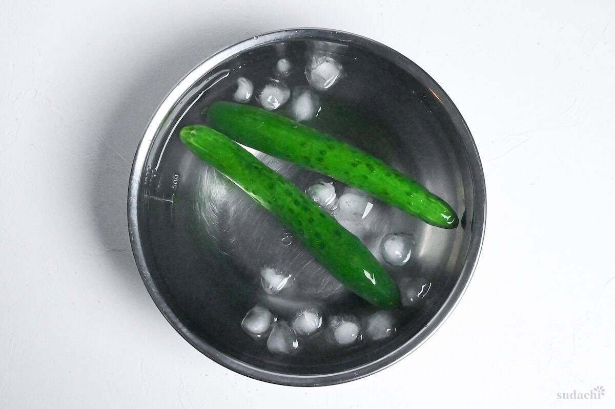 two Japanese cucumbers cooling in a bowl of ice water