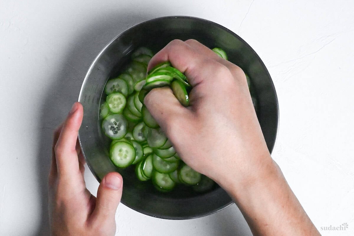 squeezing liquid out of thinly sliced Japanese cucumbers