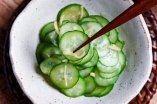 Japanese cucumber sunomono with ginger in a white mottled bowl with wooden chopsticks holding up a few slices