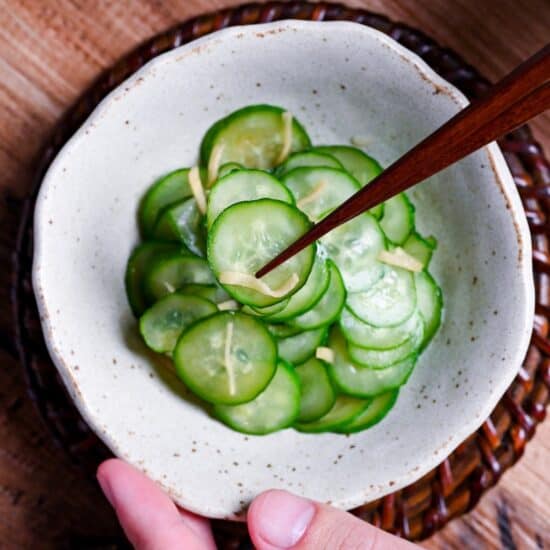 Japanese cucumber sunomono with ginger in a white mottled bowl with wooden chopsticks holding up a few slices