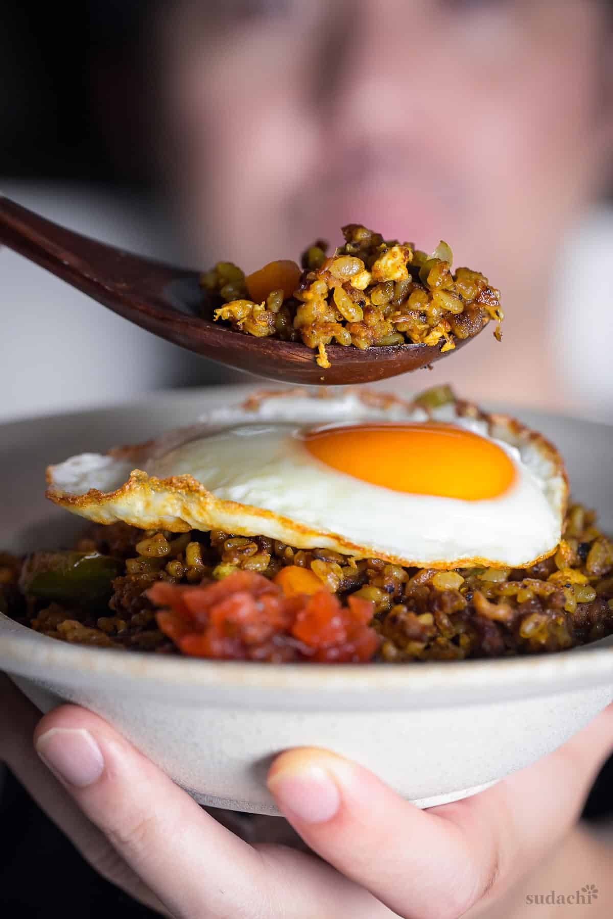 Yuto Omura holding up a white bowl of Japanese style curry rice topped with a fried egg and a spoonful held above it